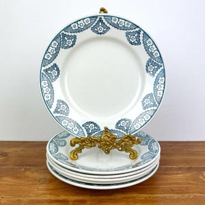 Pode incluir: Um conjunto de pratos de cerâmica branca com uma borda floral azul. Os pratos são empilhados em um suporte decorativo dourado. Os pratos são exibidos em uma superfície de madeira. Os pratos são de estilo vintage.