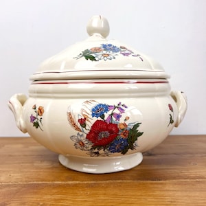 Può includere: Zuppiera in ceramica color crema con coperchio, ornata da un motivo floreale con papaveri rossi, fiordalisi blu e altri fiori colorati. La zuppiera ha due manici e un bordo rosso, perfetta per servire zuppe e stufati.
