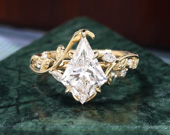 Pode incluir: Um anel de ouro com uma grande pedra preciosa transparente em forma de pipa como peça central. O anel apresenta um design inspirado na natureza com detalhes delicados de folhas e videiras, e pedras de acento menores.