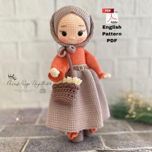 May include: A crocheted doll with a gray head covering, orange sweater, and gray skirt. The doll has a small brown purse and is holding a small bouquet. The image includes the text "English Pattern PDF".