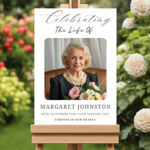 May include: A white memorial sign with a black border and a photo of a woman holding a bouquet of flowers. The sign reads "Celebrating The Life Of Margaret Johnston 06th September 1950 - 24th January 2025 Forever In Our Hearts."