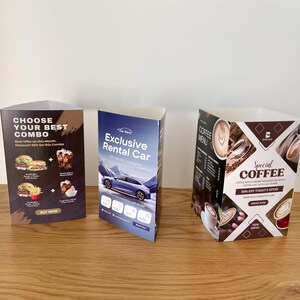 May include: Three tabletop display stands with different designs. The first stand has a brown background with a burger and fries combo, the text "Choose Your Best Combo", and the text "Buy Now". The second stand has a blue background with a car, the text "Exclusive Rental Car", and the text "Car Rent". The third stand has a brown background with coffee cups, the text "Special Coffee", and the text "Coffee Menu".