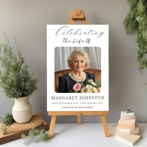 May include: A white memorial sign with a black border and a photo of a woman with a bouquet of flowers. The text reads "Celebrating The Life Of Margaret Johnston 06th September 1950 - 24th January 2025 Forever In Our Hearts."