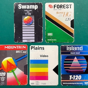 May include: A collection of five vintage VHS video cassette tapes. The tapes feature colorful designs and text, including "Swamp," "Forest," "Mountain," "Plains," and "Island." Each tape has a unique graphic and color scheme.