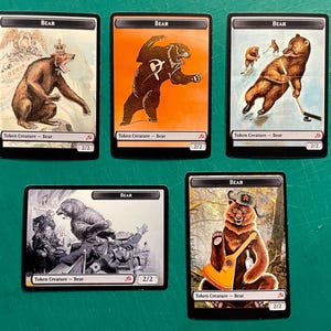 May include: Five rectangular trading cards featuring bear illustrations. Each card displays the text Bear at the top and Token Creature - Bear at the bottom with 2/2 stats. The artwork depicts bears in various settings, including playing hockey and wearing hats.