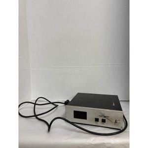 May include: A black and silver electronic device with a power cord. The device has a black top and a silver front panel with a small display screen and buttons labeled "RESET" and "EXIT". The words "Vapor Systems" are printed on the front.