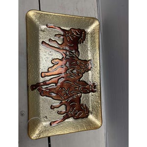 May include: Rectangular glass tray with a gold-colored textured background and a brown horse design. The horses are depicted in a stylized, artistic manner, with details in a darker brown hue. The tray has a slightly raised edge.