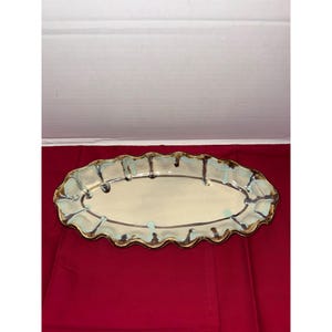 May include: An oval ceramic serving platter with a cream-colored center and a wavy, light blue and brown rim. The platter has a unique, handcrafted appearance, suitable for serving appetizers or desserts.