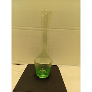 May include: A clear glass vase with a green base and a long, slender neck. The vase is approximately 18 cm tall. The vase is sitting on a black surface.