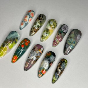 May include: A collection of ten long, almond-shaped artificial nails. Each nail features a unique abstract design with a glossy finish. Colors include green, orange, yellow, blue, and purple, creating a vibrant and artistic display.