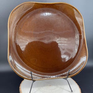 Könnte beinhalten: Ein quadratischer Keramikt quadratischer Keramikt quadratischer Keramikteller mit abgerundeten, wellenförmigen Kanten und einer glänzenden, dunkelbraunen Glasur. Die Oberfläche weist ein glattes, reflektierendes Finish mit subtilen Farbvariationen in der Mitte und am Rand auf.