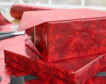 May include: Two red gift boxes wrapped in floral patterned paper. A roll of matching wrapping paper and a pair of scissors are visible. A black ribbon is draped across the surface, suggesting the gifts are ready to be presented.