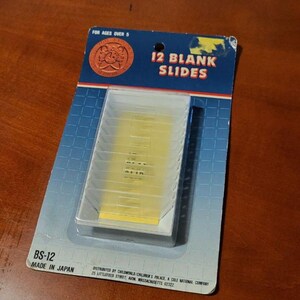 May include: A package of 12 blank slides for ages over 5. The package is blue and white with the text "12 BLANK SLIDES" in red and white. The slides are in a clear plastic container. The package is labeled "BS-12 MADE IN JAPAN".