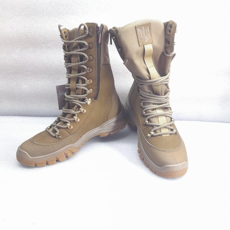 May include: A pair of brown leather military boots with a zipper on the side and a gold-colored trident logo on the top of the boot.