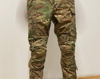 May include: Camouflage cargo pants with multiple pockets and knee pads. The pants are a blend of green, brown, and tan.