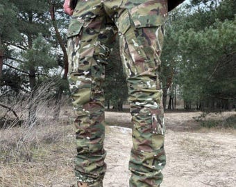 May include: Camouflage cargo pants with multiple pockets and a slim fit. The pants feature a mix of green, brown, and tan colors. Paired with tan combat boots with brown laces. The pants are designed for outdoor activities.