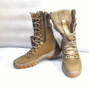 May include: A pair of brown leather military boots with a zipper on the side and a gold embroidered symbol on the top of the boot.