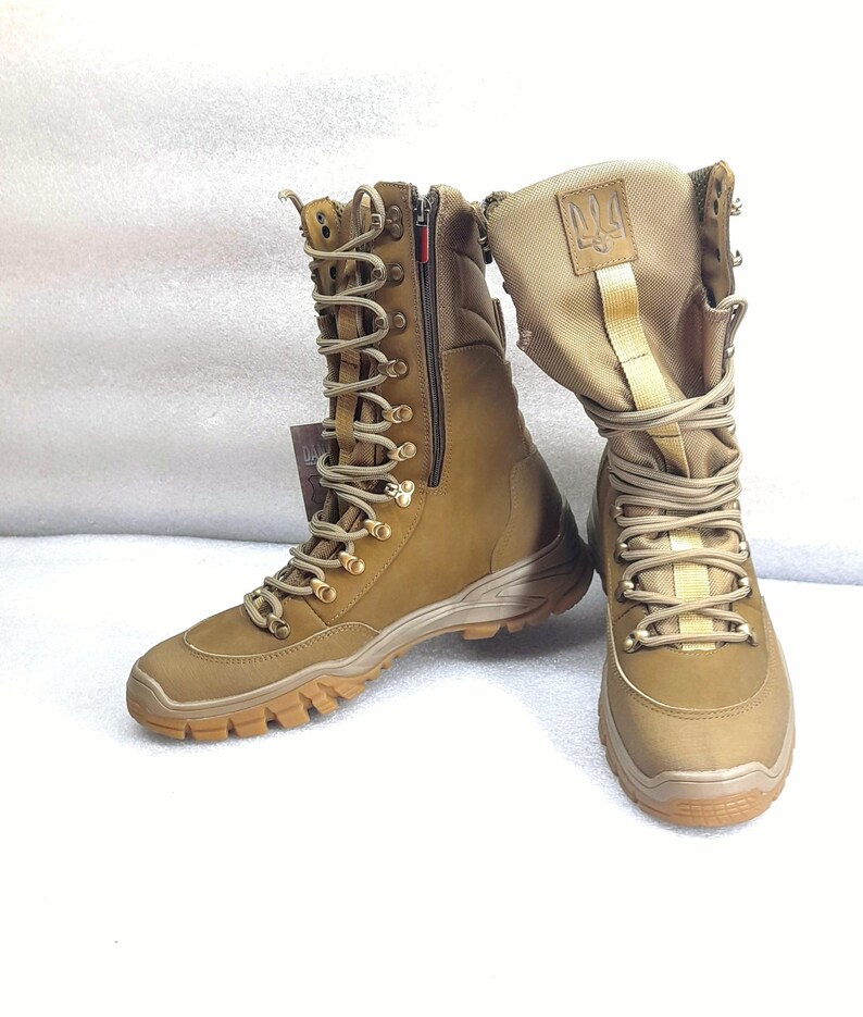 May include: A pair of brown leather military boots with a zipper on the side and a gold embroidered symbol on the top of the boot.