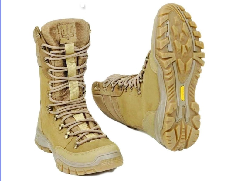 May include: A pair of tan leather military boots with a yellow sole and a trident logo on the side. The boots have a lace-up closure and a high top.