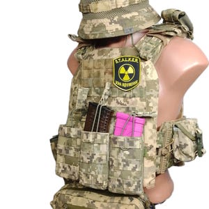 May include: A tactical vest and matching hat in a digital camouflage pattern. The vest has multiple pouches, a patch with a radiation symbol, and the text "S.T.A.L.K.E.R. ЗОНА ВИЛУЧЕННЯ". The hat has cat ears.