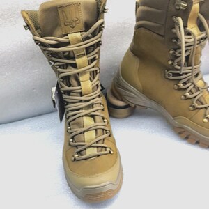 May include: A pair of tan leather hiking boots with black laces and a black logo on the side. The boots have a thick rubber sole and are designed for outdoor use.