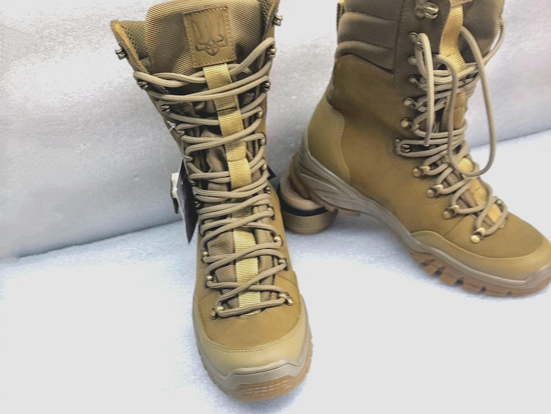 May include: A pair of tan leather hiking boots with black laces and a black logo on the side. The boots have a thick rubber sole and are designed for outdoor use.