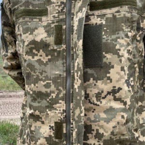 May include: A camouflage jacket with a full-length zipper and a hood. The jacket features a digital camouflage pattern in shades of green, brown, and tan. It has multiple pockets and patches, and is designed for outdoor use.