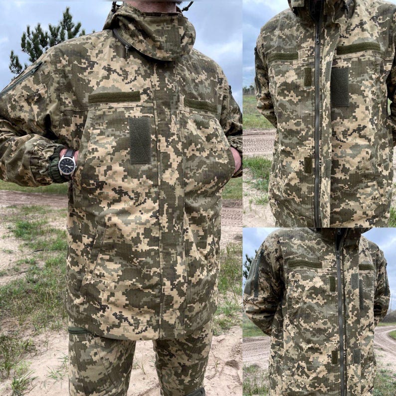 May include: A camouflage jacket and pants set in shades of green, brown, and tan. The jacket features a hood, multiple pockets, and a zipper closure. The pants have a matching camouflage pattern. The outfit is designed for outdoor use.