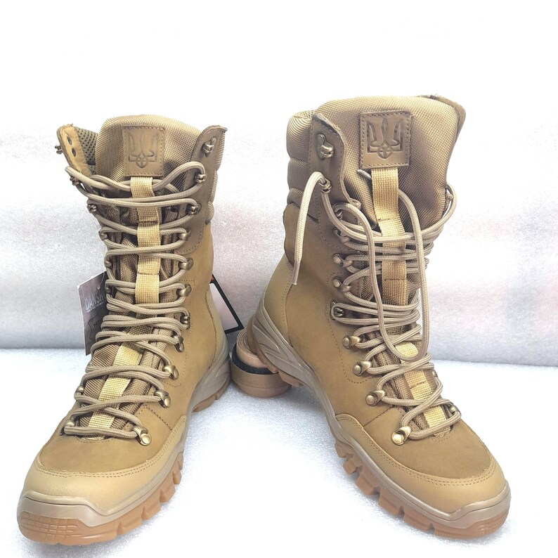 May include: A pair of tan leather hiking boots with a yellow and black lace-up closure. The boots have a thick rubber sole and a small embroidered emblem on the side.