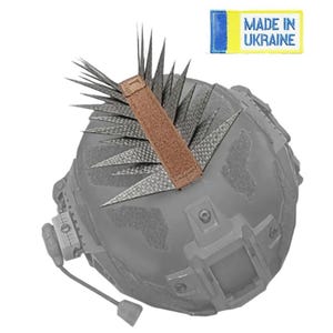 May include: A gray tactical helmet with a brown strap and spiky attachments. The helmet has a headset and the text "MADE IN UKRAINE" on a yellow and blue patch.