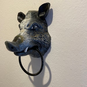Könnte beinhalten: Ein schwarzer und weißer gusseiserner Wildschwein-Kopf-Wandhalter mit einem schwarzen Metallring im Maul.