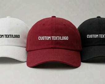 May include: Three baseball caps in white, burgundy, and black. Each cap has a curved brim and the text "CUSTOM TEXT/LOGO" embroidered in white across the front. The caps are displayed against a neutral background.
