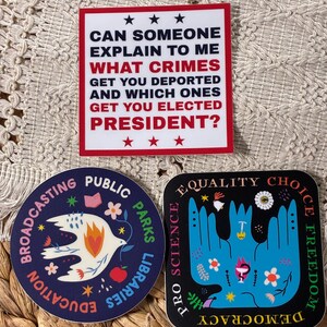 Op de afbeelding: Drie stickers met politieke en sociale rechtvaardigheidsthema's. E&eacute;n leest: "Kan iemand mij uitleggen welke misdaden ervoor zorgen dat je wordt gedeporteerd en welke ervoor zorgen dat je tot president wordt gekozen?" Een andere zegt "Broadcasting Public Parks Libraries Education". De derde zegt "Equality Choice Freedom Pro Science Democracy".