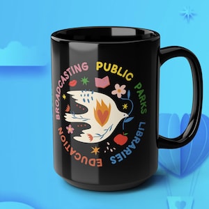 May include: Black ceramic mug with a white dove graphic holding a sprig, surrounded by text and colorful illustrations. The mug features the words "Broadcasting, Public, Parks, Libraries, Education."