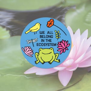 May include: A round, blue sticker with the text "WE ALL BELONG IN THE ECOSYSTEM." The sticker features illustrations of a yellow bird, a dragonfly, a frog, a flower, and other botanical elements. The sticker is set against a background of a pink water lily and green lily pads.