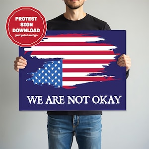 May include: A rectangular sign featuring a stylized American flag design with red and white stripes and blue stars. The words "WE ARE NOT OKAY" are printed in white. A red and white circular sticker says "PROTEST SIGN DOWNLOAD just print and go".
