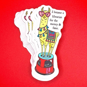 May include: A stack of white stickers with a yellow llama wearing heart-shaped glasses. The llama stands on a red and blue stand and is decorated with tassels and a colorful blanket. Text reads, "I became a librarian for the money & fame."