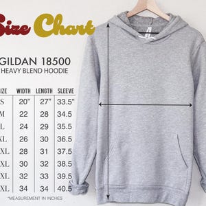 Pode incluir: Um moletom cinza claro Gildan 18500 Heavy Blend em um cabide de madeira. A imagem inclui uma tabela de tamanhos com medidas em polegadas para largura, comprimento e comprimento da manga, variando do tamanho S ao 5XL. A largura do tamanho S &eacute; de 50,8 cm.