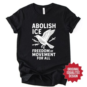 May include: Black t-shirt with a white graphic of a bird breaking through barbed wire, with the words "ABOLISH ICE" and "FREEDOM OF MOVEMENT FOR ALL". The shirt also has a red star-shaped design that says "ORIGINAL EQUALITEE DESIGN".