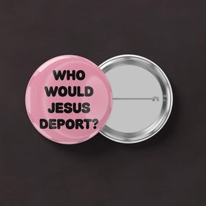 May include: A pink button with the text "WHO WOULD JESUS DEPORT?" in black. The button is next to a silver-colored button back with a pin.