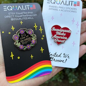 Pu&ograve; includere: Due spille smaltate su cartoncini. Una spilla &egrave; a forma di cuore con la scritta "Immigrants Make America Great". L'altra spilla &egrave; una ghirlanda floreale con la scritta "Big Fan of Human Rights". I cartoncini hanno il marchio "EQUALITE".