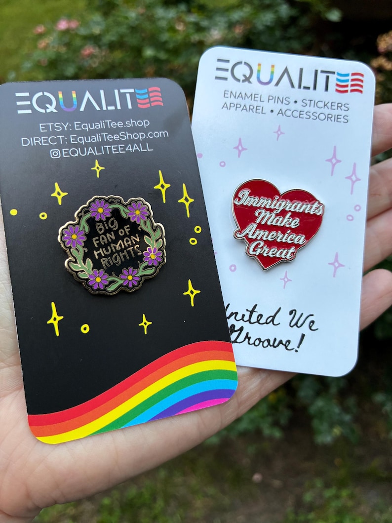 Pu&ograve; includere: Due spille smaltate su cartoncini. Una spilla &egrave; a forma di cuore con la scritta "Immigrants Make America Great". L'altra spilla &egrave; una ghirlanda floreale con la scritta "Big Fan of Human Rights". I cartoncini hanno il marchio "EQUALITE".