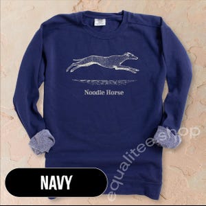 Pode incluir: Camisola azul marinho com um gr&aacute;fico branco de um c&atilde;o a correr e o texto "Noodle Horse". A camisola tem gola redonda e punhos canelados. A palavra "NAVY" &eacute; exibida num ret&acirc;ngulo preto na parte inferior.