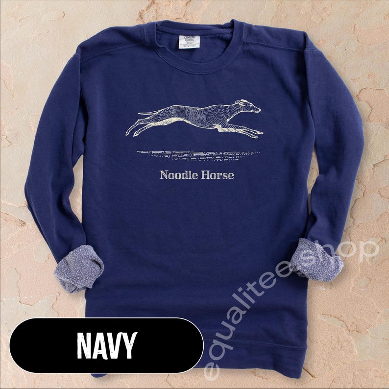 Pode incluir: Camisola azul marinho com um gr&aacute;fico branco de um c&atilde;o a correr e o texto "Noodle Horse". A camisola tem gola redonda e punhos canelados. A palavra "NAVY" &eacute; exibida num ret&acirc;ngulo preto na parte inferior.