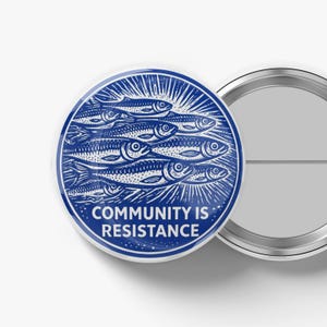 May include: A round, blue and white button with the text "COMMUNITY IS RESISTANCE". The button features a graphic of several fish swimming together, with radiating lines emanating from behind them. A second button is partially visible.