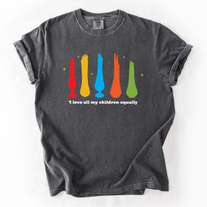May include: Dark gray t-shirt with a colorful graphic of abstract shapes in red, yellow, blue, orange, and green. The text "I love all my children equally" is printed below the graphic. The shirt has rolled-up sleeves.