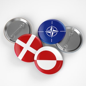 May include: A collection of round pinback buttons. One button features the NATO symbol on a blue background. Other buttons display the flags of Denmark and Greenland, with a silver pin on the back.