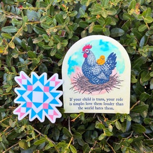 May include: Two stickers on a green leafy background. One sticker features a blue, pink, and white geometric design. The other sticker shows a hen with a chick, a nest, and the text: "If your child is trans, your role is simple: love them louder than the world hates them."
