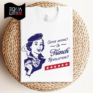 May include: White t-shirt with a blue illustration of a woman in a beret holding a cup of coffee. The text reads "Coffee anyone? Or French Revolution?" with five red stars below.