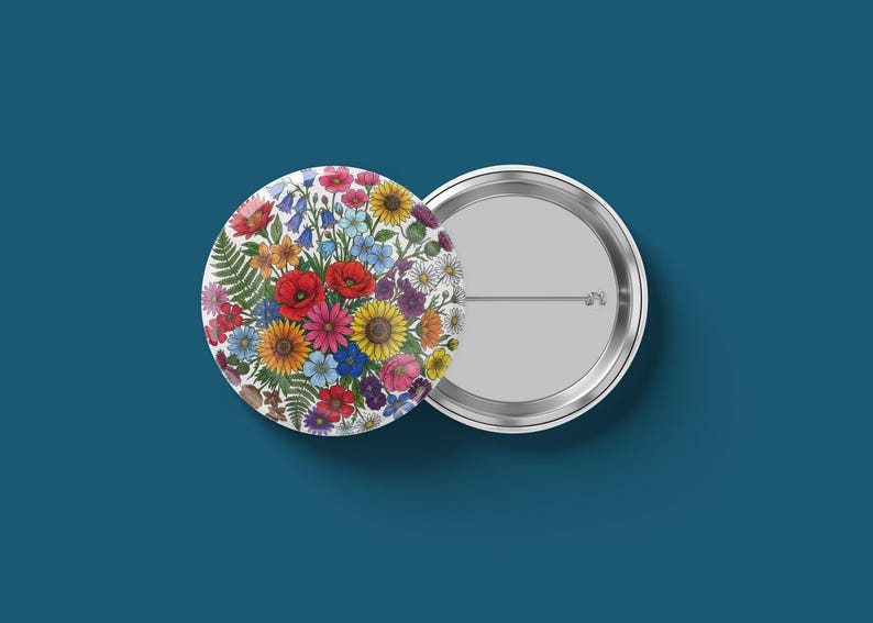 May include: Two round pinback buttons. One button features a colorful floral design with red poppies, yellow sunflowers, and bluebells. The other button is silver with a pin on the back. The background is a solid teal color.